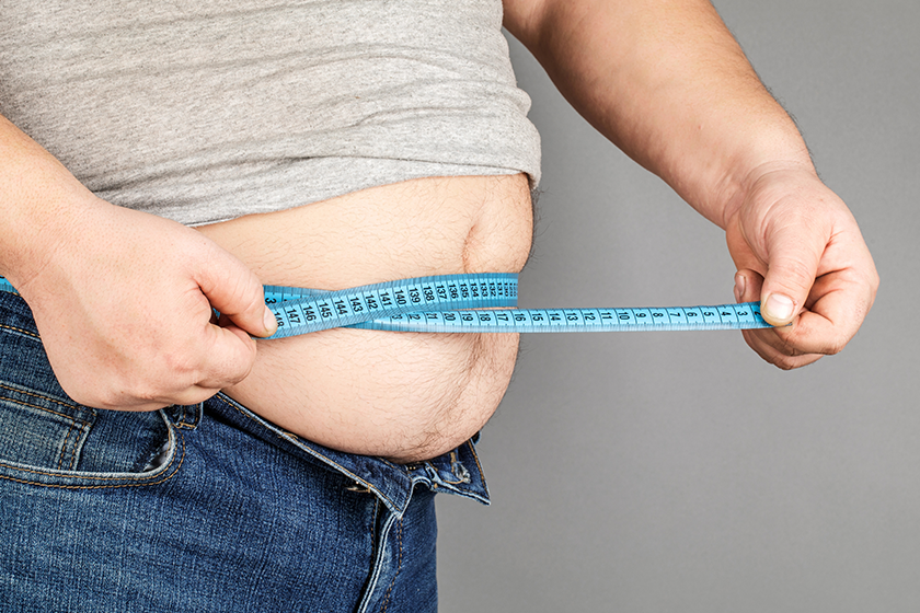 A man measures his fat belly with a measuring tape. on a gray ba