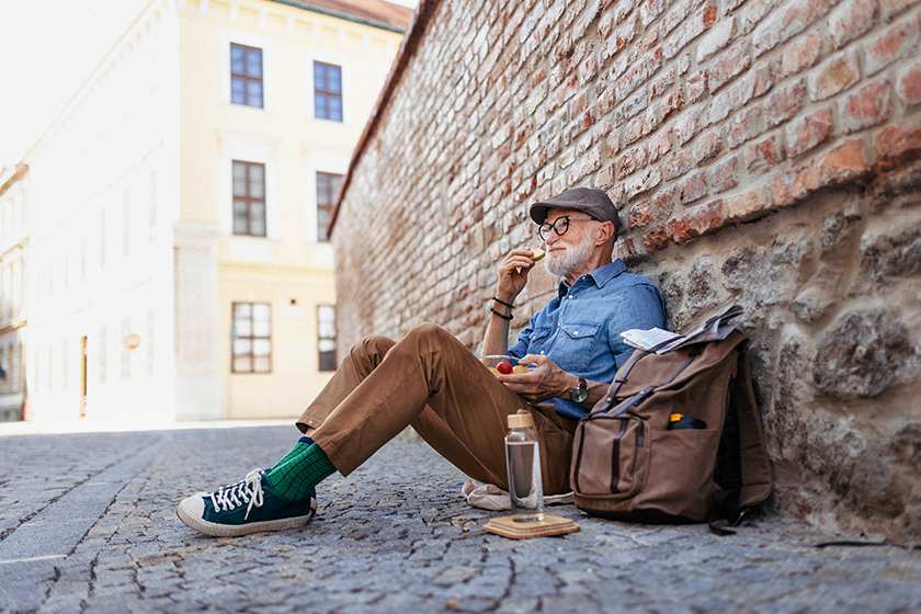 Elderly man with backpack sitting by the brick wall
