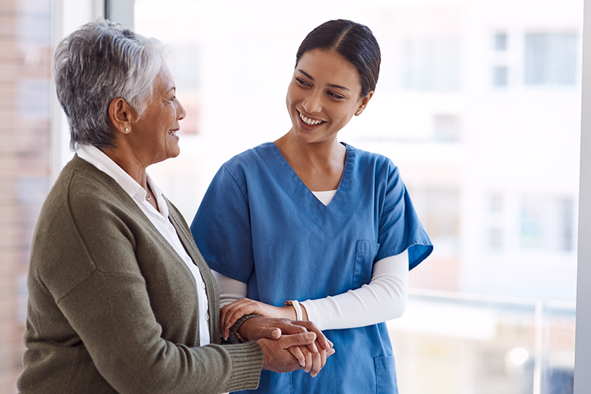 Support, caregiver with senior woman and holding hands for care indoors. Retirement, consulting and professional female nurse with elderly person smiling together for healthcare at nursing home.